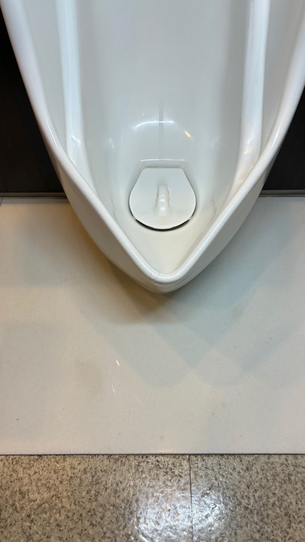 白っぽい色の汚垂石。小便器の下から外側へ広がるように黄ばみが出ている様子